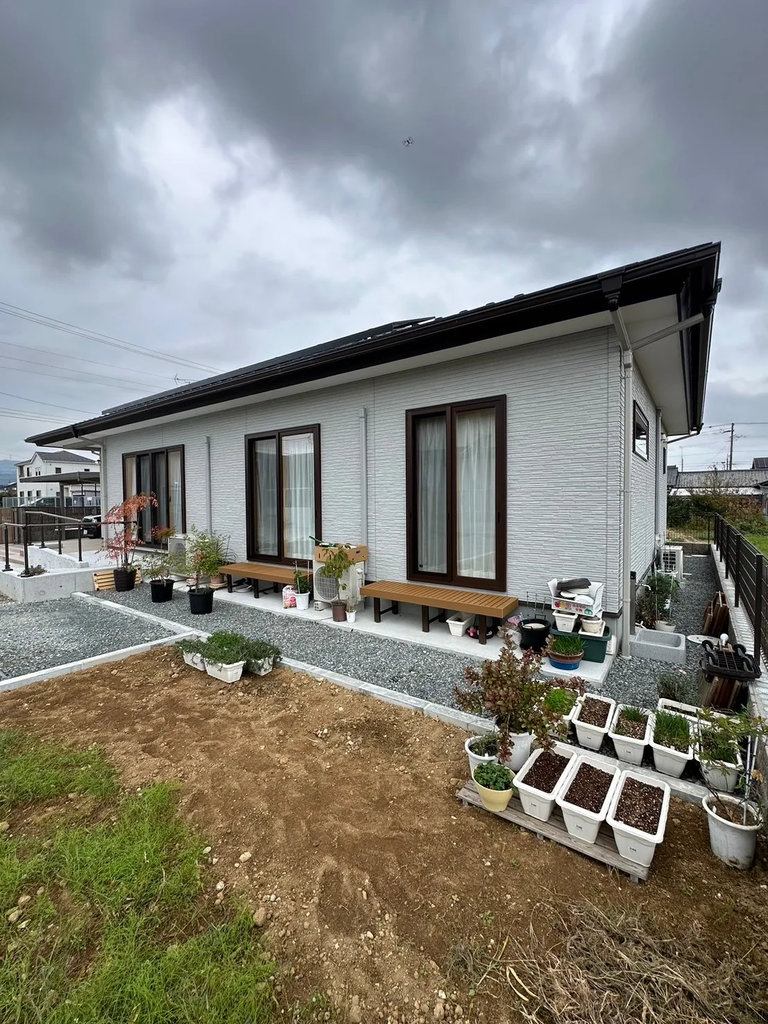 白い外壁と深い軒、掃き出し窓に沿うウッドデッキのある平屋の外観