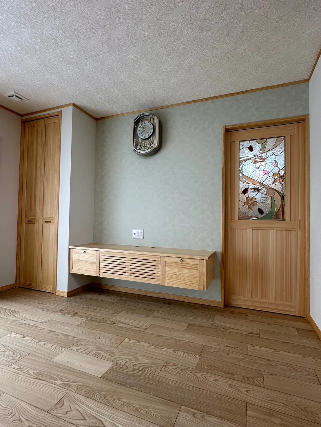 造作の壁掛け収納とステンドグラス入りの木製建具がある室内